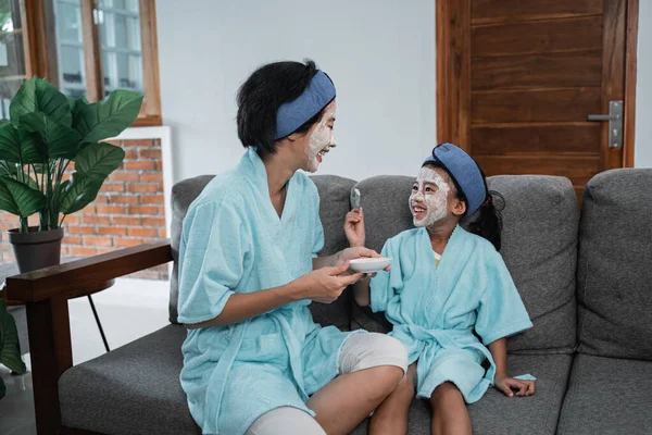 En mor och hennes lilla flicka leende bär en kräm ansiktsmask bär en handduk och pannband — Stockfoto