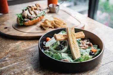 Siyah tabakta taze sebze salatası ve sosisli sandviç.