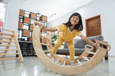 Pikler üçgeninde denge oynarken küçük kız gülümsüyor