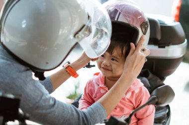 Annesi ona yardım ederken bebek motosiklet kaskı takıyor.