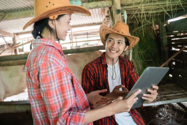 İki inek çiftçisi birlikte bir tablet kullanarak bir açıklama yapıyor.