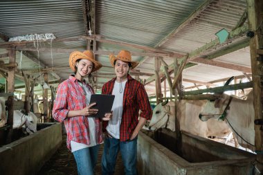 Dijital tablet taşıyan çiftçi bir iş ortağıyla kameraya bakan gülümseyen bir adam.
