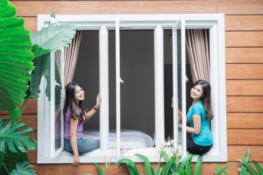 İki güzel ikiz kardeş evde, pencerenin yanında duruyor.