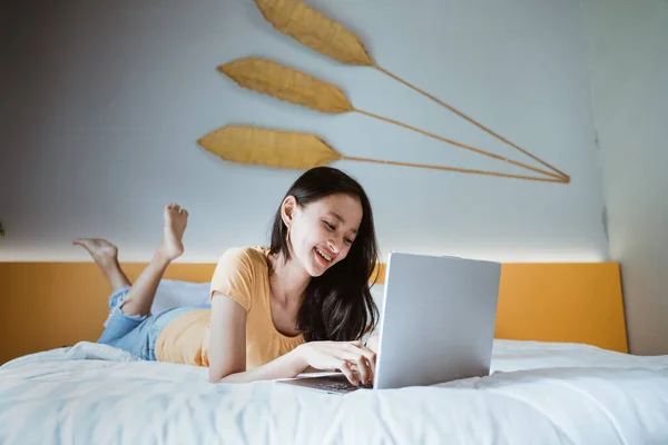 Egy nő fekszik az ágyon a laptopja előtt. Otthonról dolgozom a karanténban. Társadalmi elszigeteltség — Stock Fotó