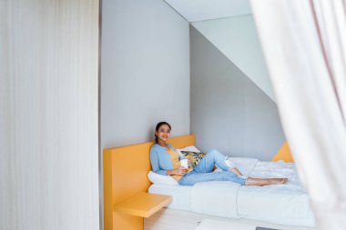 Asyalı kadın rahat yatak odasında kahve içiyor. Sabah ritüelleri.