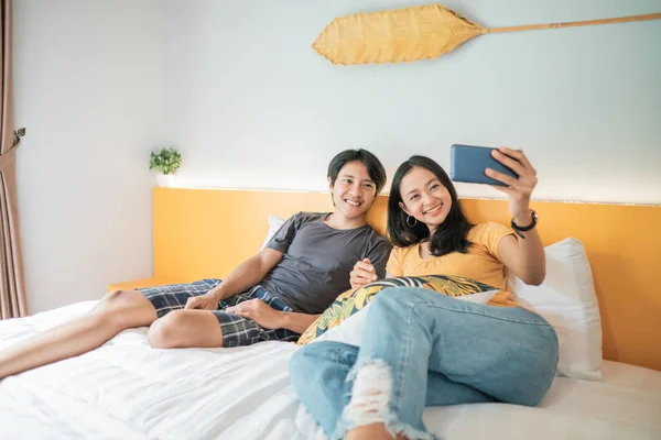 Pár használ okos telefon és mosolygós, miközben időt az ágyban otthon — Stock Fotó