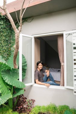 Ekose gömlekli ve kot pantolonlu bir adam pencerenin yanında durup düşünüyor.