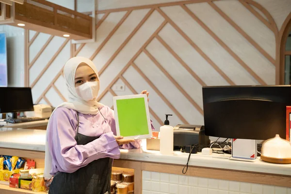 businesswoman wear head scarf and mask standing at her store showing blank tablet pc