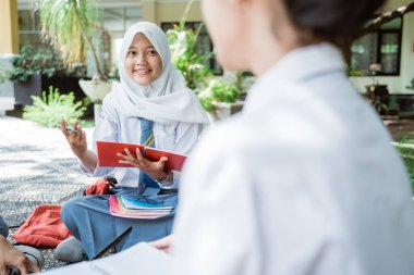 Endonezya 'da tesettüre girmiş bir kız öğrenci el hareketleriyle gülümser ve bir grupta çalışırken bir kitap tutar.