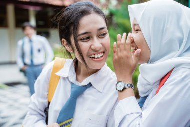 Kız arkadaşı erkek arkadaşı hakkında fısıldarken gülümseyen bir lise öğrencisinin fotoğrafını çek.