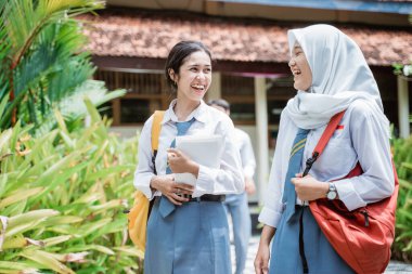 Okul çantaları takıp gülen ve okul binalarıyla yürüyen iki liseli kızın fotoğrafını çekeceğim.