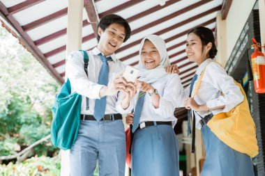 Üç Asyalı lise öğrencisi bilgi almak için bir cep telefonu kullanıyor.