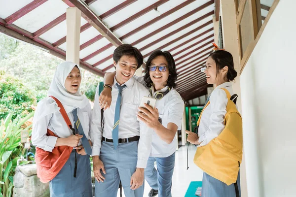 Dört lise öğrencisi bilgi almak için bir cep telefonu kullanıyor.