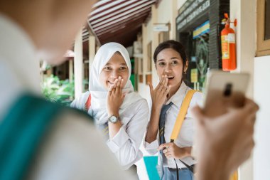 Bir öğrenci cep telefonu ekranı gösterdiğinde şok olmuş iki lise öğrencisi.