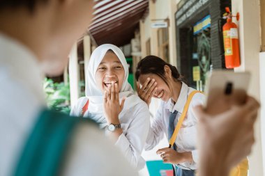Bir öğrenci akıllı telefon ekranı gösterdiğinde gülen iki liseli kız.