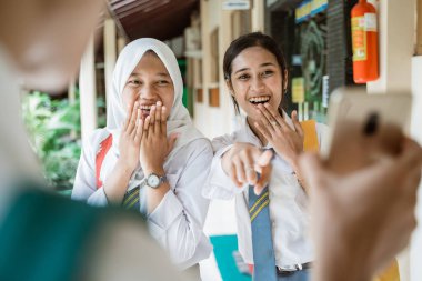 Gülen ifadeleri ve akıllı telefonu işaret eden iki liseli kız.