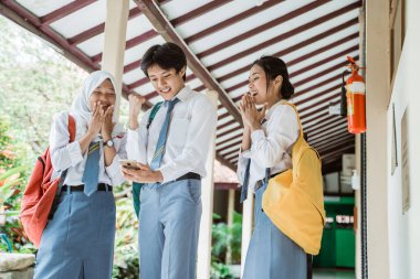 Üç lise öğrencisi mezuniyet ilanını görmek için bir akıllı telefon kullanarak ekrana bakıyor.