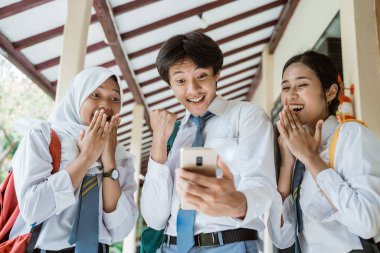 Mezuniyet ilanını görmek için ekranda bir akıllı telefon kullanarak üç lise öğrencisini kapatın.