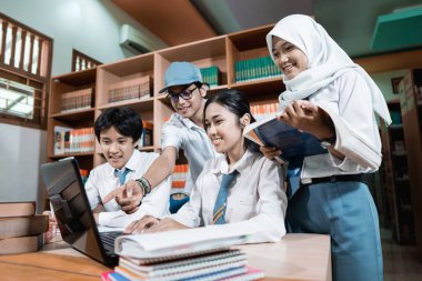 Dört lise öğrencisi dizüstü bilgisayar kullanıyor ve bir tanesi de birlikte masa başında çalışırken ekranı işaret ediyor.