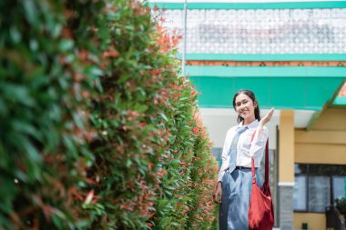 Endonezyalı bir öğrenci gülümsüyor Endonezya 'nın lise üniforması içinde el hareketleriyle bir şeyler sunuyor.