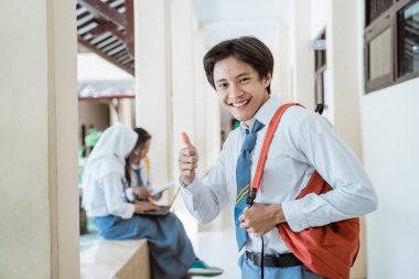 Liseli bir çocuk kameraya gülümsüyor ve okul çantası takıyor.