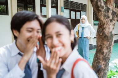 Sinirli peçeli kız lise üniformalı bir kıza fısıldadığında