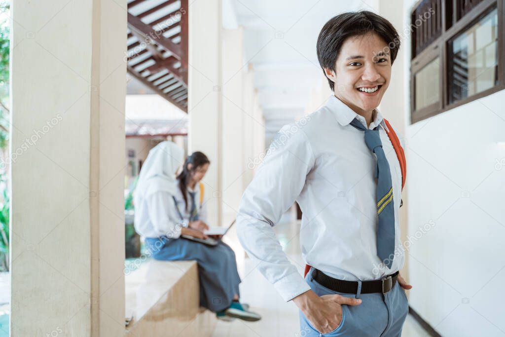 a high school boy smiles at the camera wearing a school bag