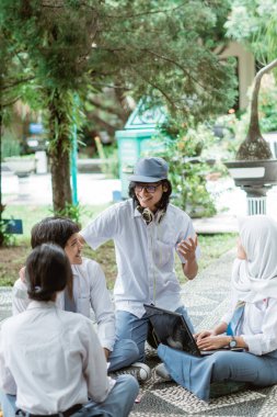 Lise üniformalı, kulaklık takan ve güneş gözlüğü takan bir öğrenci üç arkadaşıyla tanışıyor.
