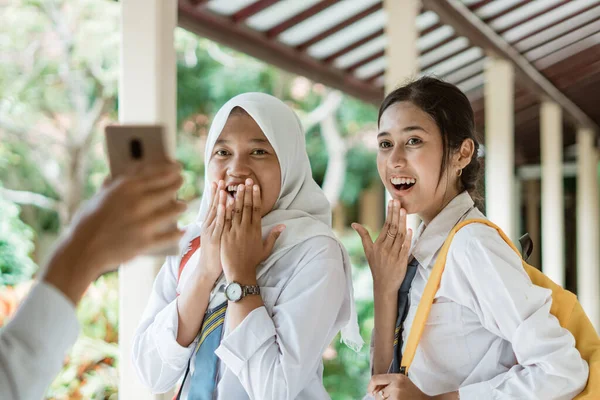 Endonezya 'da liseli üniformalı iki kız. Bir oğlan akıllı telefon ekranı gösterdiğinde şok olmuş bir ifade takınıyorlar.