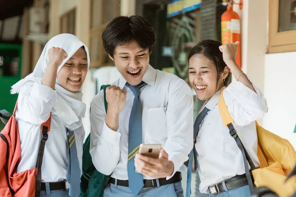 Lisedeki üç öğrenciyi hevesle kapatın. Ortak duyuruları izlemek için bir akıllı telefon kullanın.