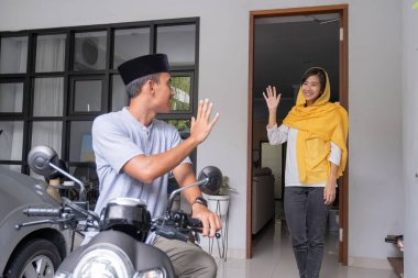 Asyalı koca motosikletle ayrılmadan önce karısına el sallıyor.