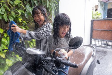 Asyalı çocuk evde motosiklet scooter 'ı yıkıyor.