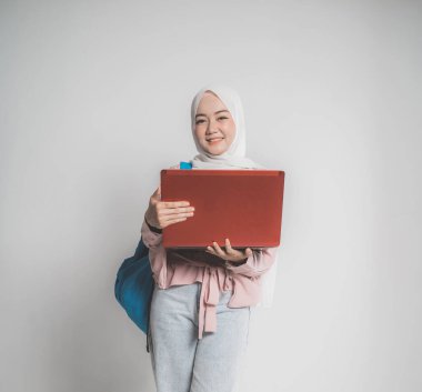 Asyalı Müslüman öğrenci dizüstü bilgisayarını beyazın önünde tutuyor.