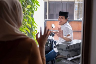 Asyalı koca motosikletle ayrılmadan önce karısına el sallıyor.