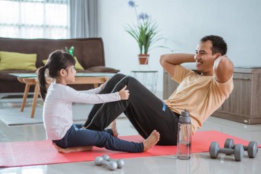 Çocuk babasına yardım ediyor. Evde oturup egzersiz yapıyor.