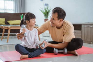Mutlu baba ve kızı birlikte halter kaldırarak egzersiz yapıyor.