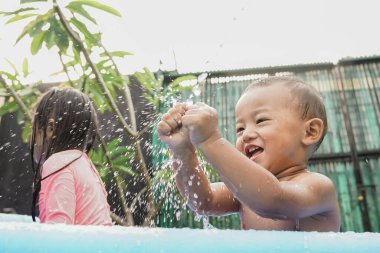 Neşeli küçük çocuk kardeşiyle açık havuzda su oyunu oynuyor.