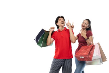 Mutlu genç Asyalı çift alışveriş torbaları getiriyor ve mutluluk ifadesiyle işaret ediyor.