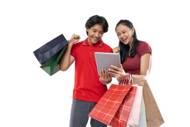Asyalı genç çift alışveriş torbaları getiriyor ve mutluluk ifadeli tablet gibi görünüyorlar.