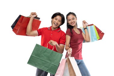 Mutlu genç Asyalı çift mutlu bir ifadeyle el kaldırırken bir sürü renkli alışveriş çantası getiriyor.