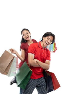 Bir sürü renkli alışveriş çantası taşıyan mutlu, genç Asyalı çift kameraya bakarken poz veriyor, mutlu bir ifade.