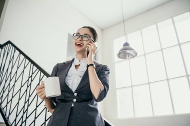 Genç ve güzel bir iş kadını telefonda konuşurken mutlu bir şekilde içki içiyor.