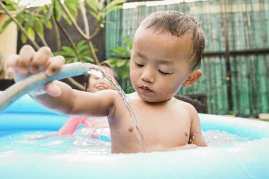 Mutlu küçük çocuk açık havuzda su hortumu oynuyor.