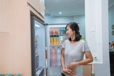 Aç genç Asyalı kadın yemek ararken karnını tut.