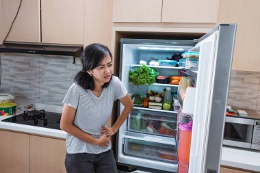 Aç genç Asyalı kadın yemek ararken karnını tut.