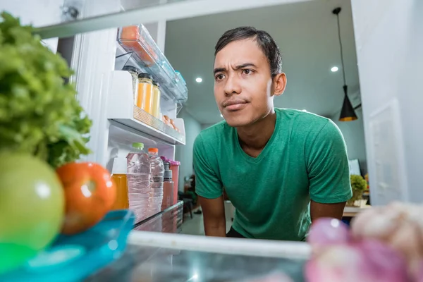 man open fridge door and confuse looking something to eat