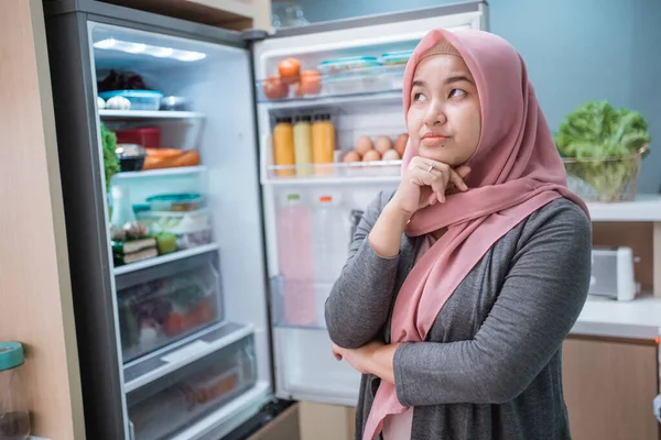 muslim asian woman thinking while open the refrigerator door before cooking