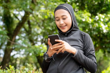 Dışarıda spor yaparken akıllı telefonunu kullanırken gülümseyen bir kadın.