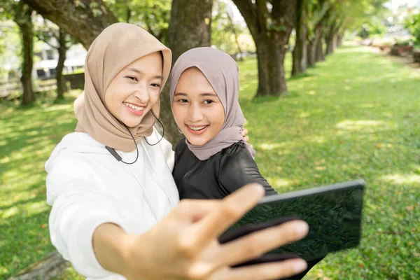 muslim friend taking selfie or video calling outdoor using her smart phone during sport break outdoor