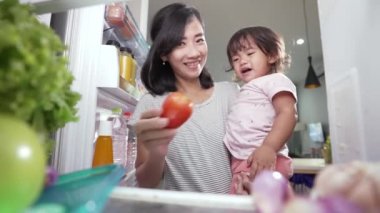 Asyalı anne kızını taşıyor. Ona biraz yemek ikram ediyor ama o reddediyor.